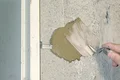 Ein Heimwerker trägt mit einer Kelle Putz auf eine Wand auf, um eine glatte, ebenmäßige Oberfläche zu schaffen.