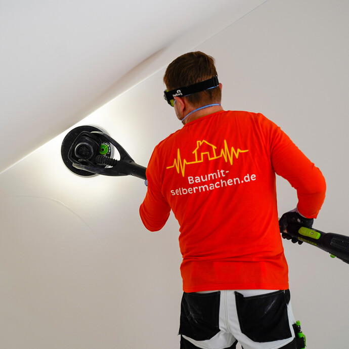 Der Heimwerker schleift die Wand mit einem Trockenbauschleifer.