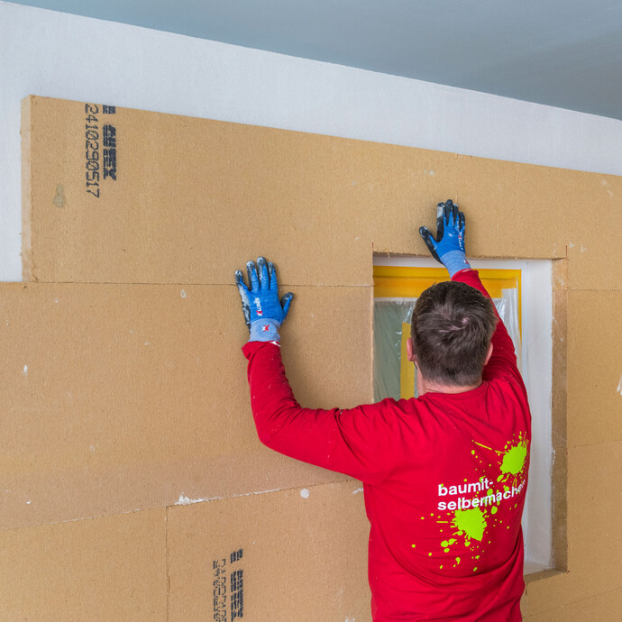 Heimwerker klebt die Holzfaserdämmplatten als Innendämmung rund um das Fenster und vervollständigt die Dämmung. Baumit Selbermachen Anleitung.