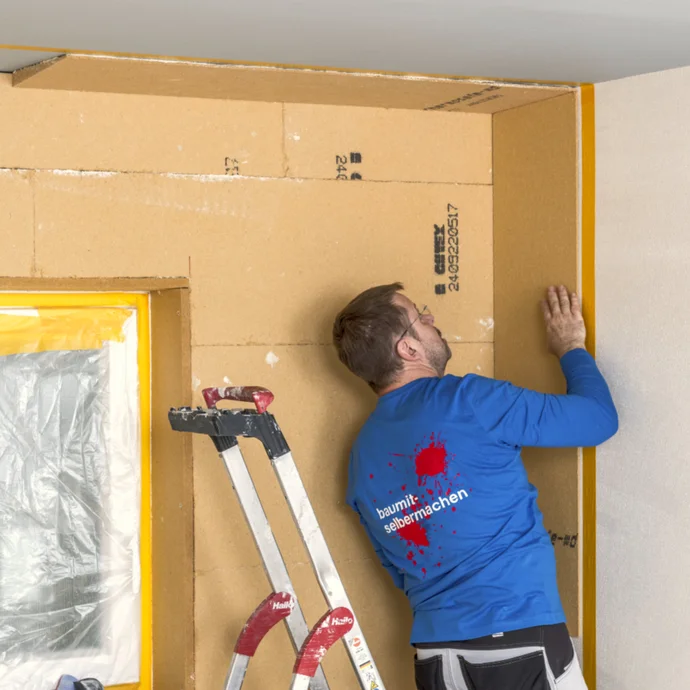Heimwerker beim Anbringen von Dämmplatten an der Wand, bereit für die finale Verkleidung, auf einer Baustelle im Innenbereich.