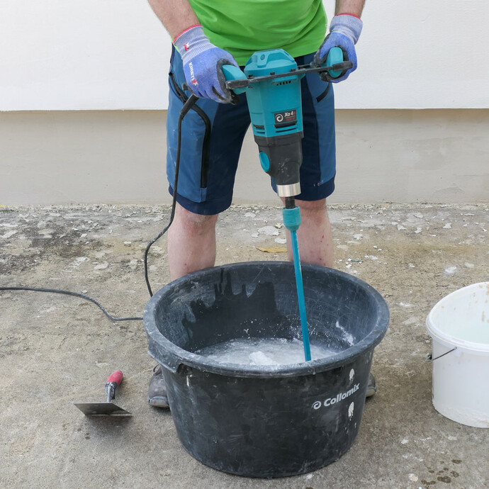 Heimwerker mischt den Münchner Rauputz mit Wasser und elektrischem Rührgerät im Mörtelkübel.