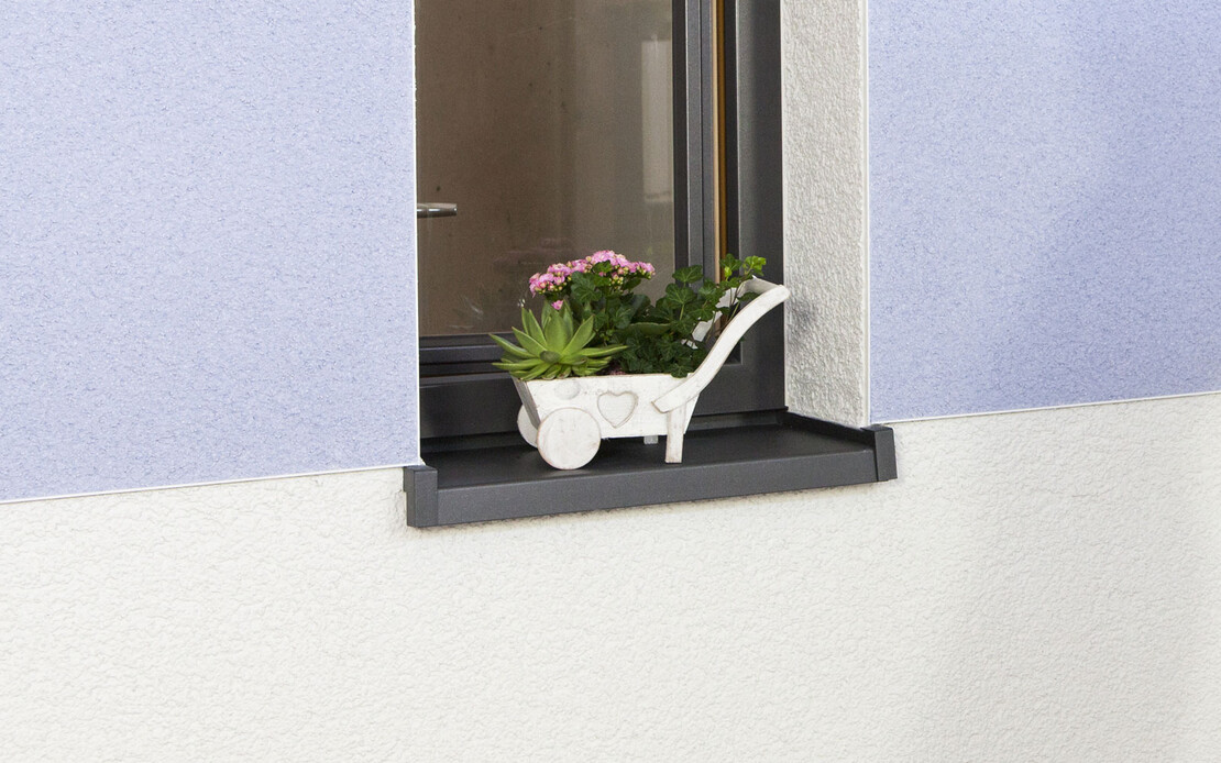 Fassade mit zweifarbigem Oberputz in Weiß und Blau, sauber verarbeitet bis zur Fensterkante. Auf dem Fensterbrett steht eine kleine Pflanze.