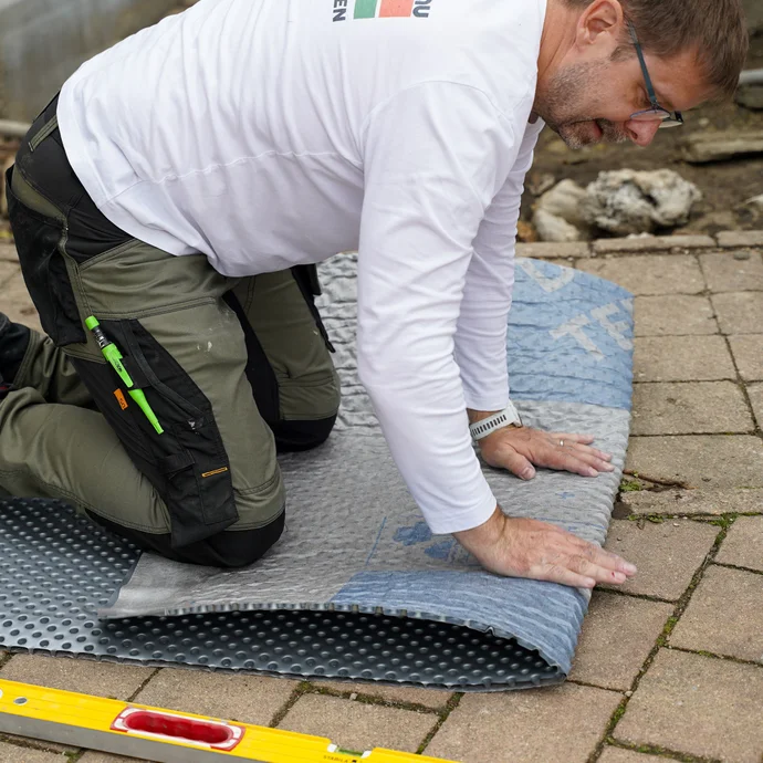 Handwerker kniet auf der Noppenbahn und knickt sie ein Mal vor.