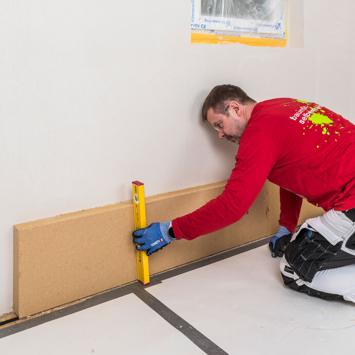 Heimwerker prüft die lotgerechte Verklebung einer Baumit Holzfaserdämmplatte mit einer Wasserwaage – Dämmplatte kontrollieren und bei Bedarf korrigieren, solange der Klebemörtel noch nicht abgebunden hat, Baumit Selbermachen Anleitung.