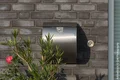 Moderner Briefkasten an einer Ziegelwand mit blühender Pflanze im Vordergrund.