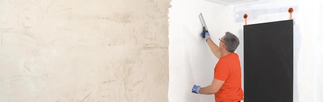 Heimwerker beim Spachteln einer Wand mit weißer Farbe; Schritt-für-Schritt-Erklärung für modernes Finish im Innenbereich.