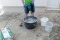 Heimwerker mischt Münchner Rauputz mit Wasser und elektrischem Rührgerät im Mörtelkübel.