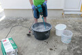 Heimwerker mischt Münchner Rauputz mit Wasser und elektrischem Rührgerät im Mörtelkübel.