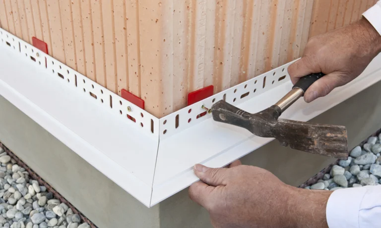 Fassadendämmung: Handwerker bringt mit Hammer und Schlagschrauber ein Sockelprofil auf gedämmter Fassade an.