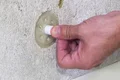 Daumen drückt Polystyrol-Dämmstoffdübel in Wandoberfläche, Schritt der Dämmstoffbefestigung erläutert.