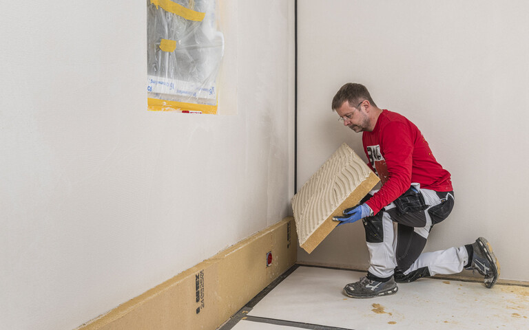 Heimwerker klebt die Holzfaserdämmplatte an die Wand. Innendämmung selber an die Wand kleben. Baumit DIY-Anleitung.