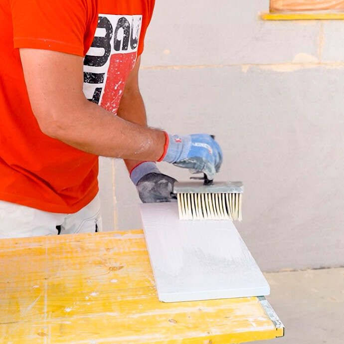 Person grundiert die Kalziumsilikat-Laibungsplatte mit einem Malerquast.