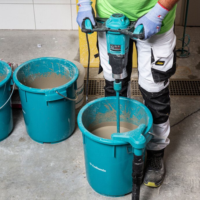 Person misch die Nivelliermasse im Eimer mit einem elektrischen Rührgerät.