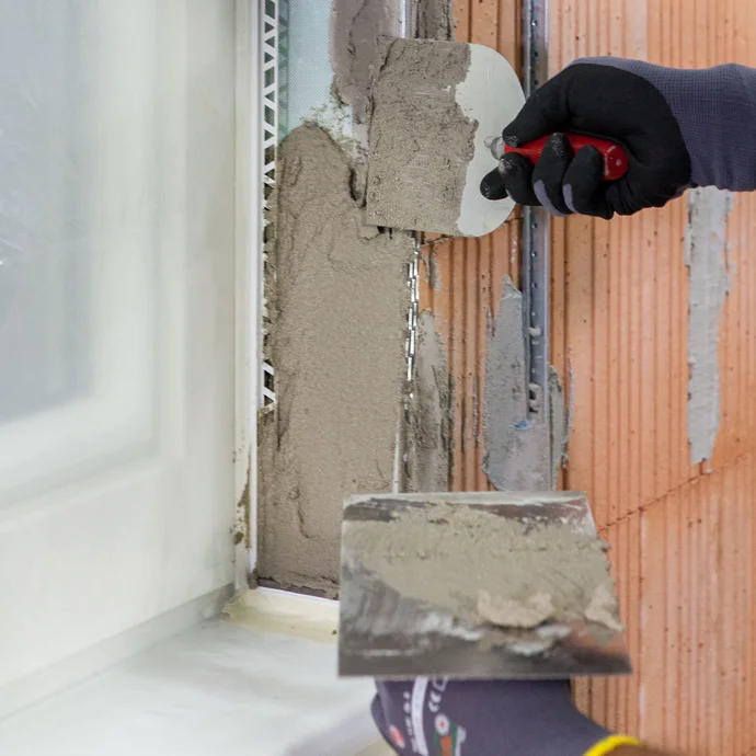 Heimwerker trägt Kalkzementputz mit einer Maurerkelle in der Fensterlaibung auf.