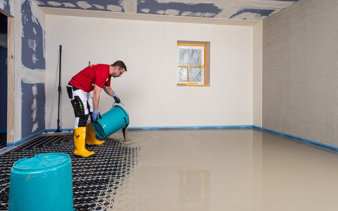 Heimwerker leert den Eimer mit Ausgleichsmasse auf die eingebaute Fußbodenheizung.