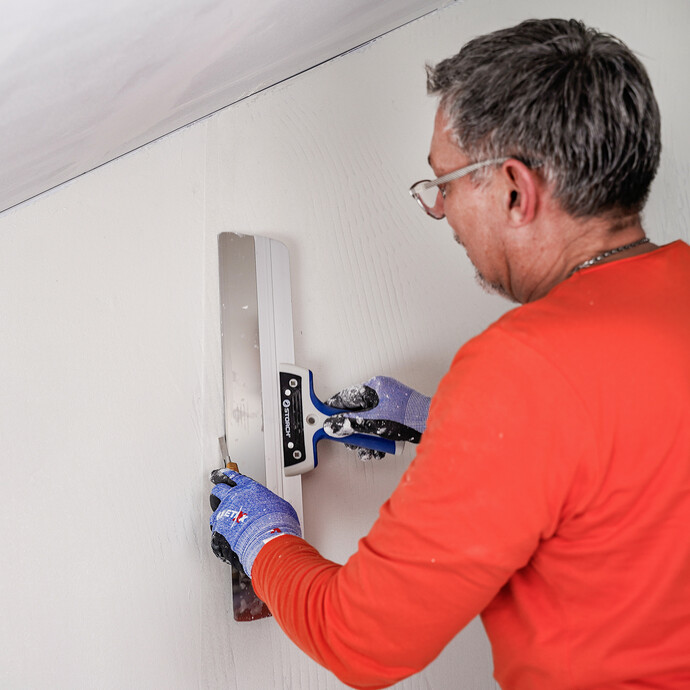 Mann führt Doppelnahtschnitt mit einem Flächenspachtel und einem Cuttermesser durch.