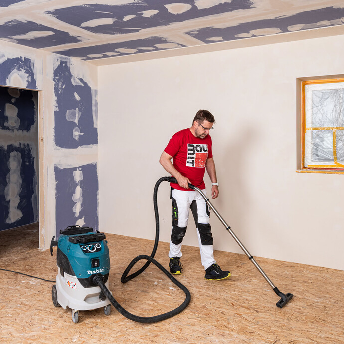 Heimwerker mit rotem Baumit T-Shirt saugt den Holzboden mit einem Industriesauger ab.