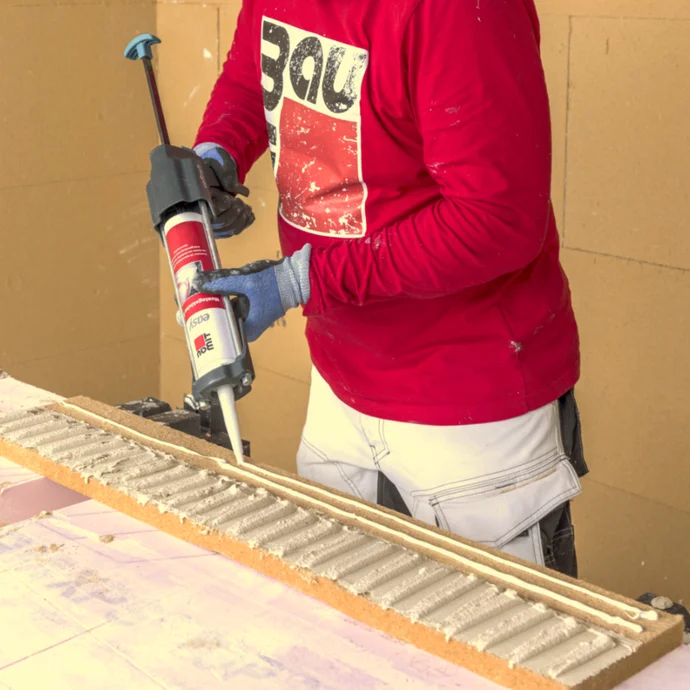 Heimwerker trägt Kleber mit einer Kartuschenpistole auf, ideal für präzise Arbeiten beim Ausbau und der Renovierung.