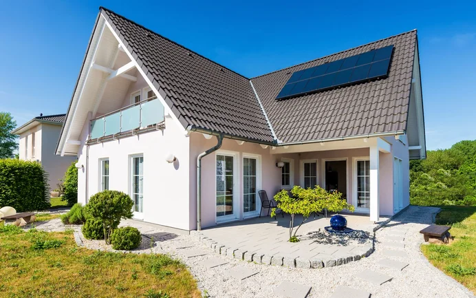 Modernes Einfamilienhaus mit Solarpanelen und gepflegtem Garten, ideal für energieeffiziente Renovierungsprojekte.