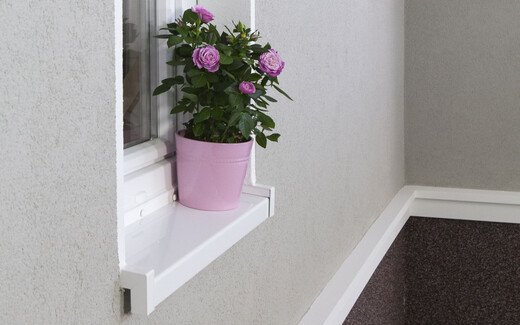 Eine Wand mit grauem Putz über und Mosaikputz unter weißen Stuckelementen. In der Wand ist ein Fenster, es steht ein Blumentopf auf dem Fensterbrett.