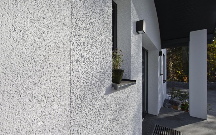 Einfamilienhaus in Weiß. Die Fassade ist mit verschiedenen Putzstrukturen mit feiner und grober Körnung gestaltet.