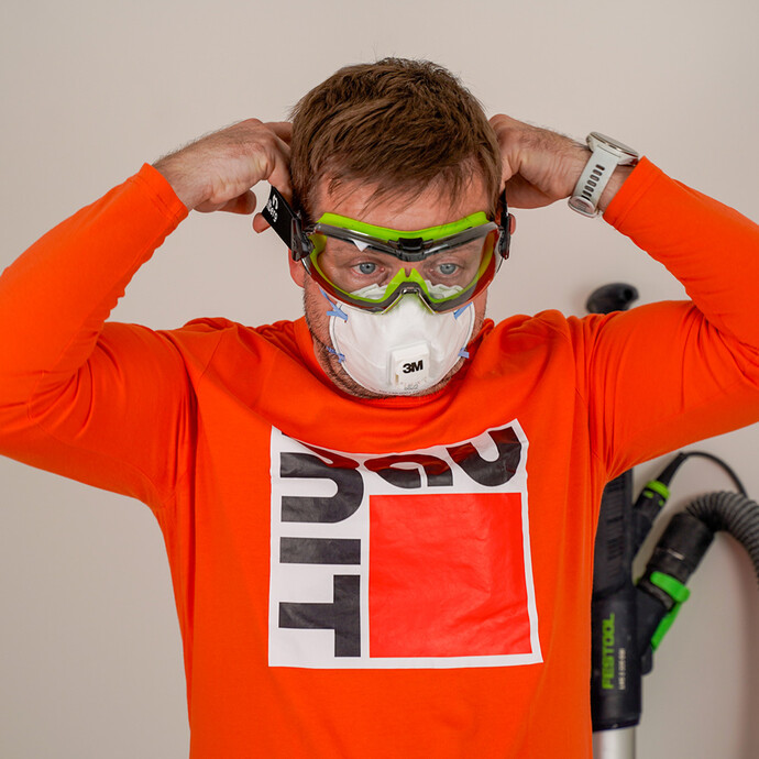 Der Heimwerker schütz sich beim Schleifen mit einer Atemschutzmaske und geschlossenen Schutzbrille.