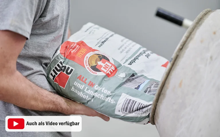 Person trägt einen Sack Baumit-ALL IN-Baustoff, geeignete Wahl für Heimwerkerprojekte im Garten- und Landschaftsbau.