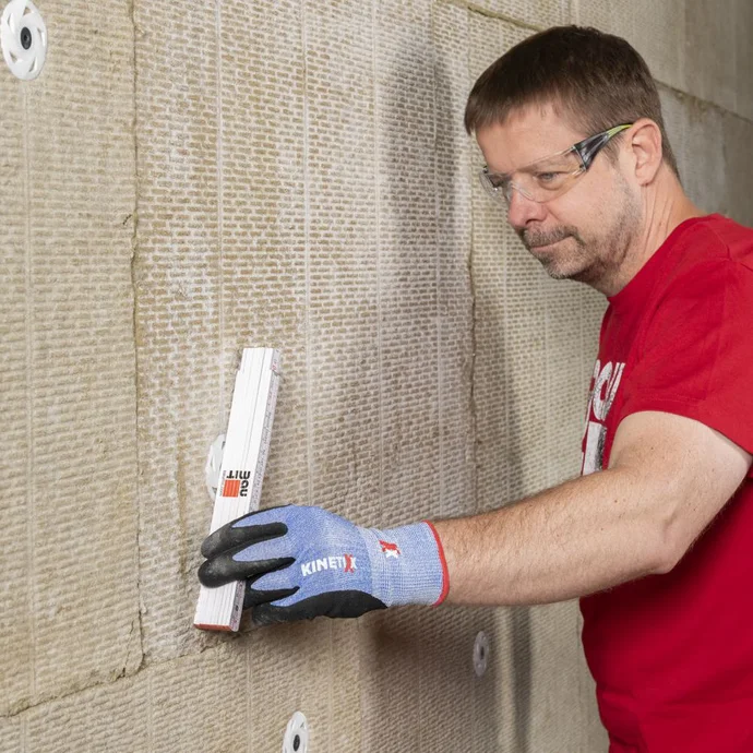 Heimwerker bringt Dämmplatte an Wand an; Baumontage in Eigenregie mit optimalem Werkzeug für bessere Isolierung.