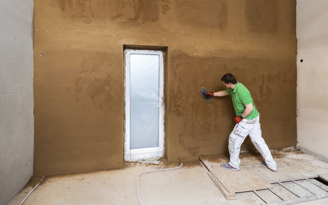 Mann rabottiert den frisch verputzten Lehmputz an einer Innenwand.