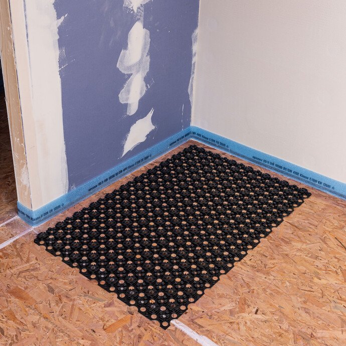 Albausanierung: Raum zur Renovierung mit Trockenbauwand und befestigtem Randdämmstreifen. Die Noppenbahn Minitec liegt auf dem Holzboden positioniert in der Ecke des Raums.