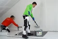Der Airless- und Rollspachtel Silikat wird von einer Person mit der Walze aufgetragen und die andere Person glättet den Spachtel ab.
