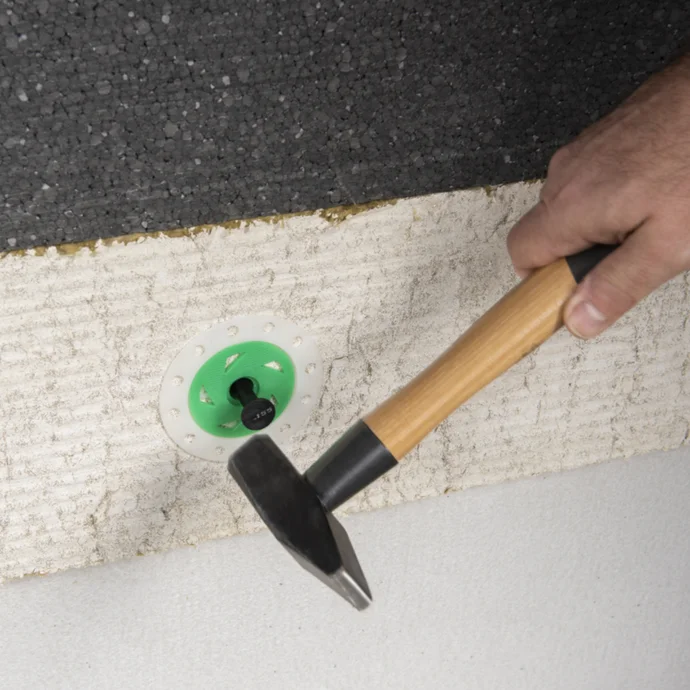 Person befestigt Dämmstoffplatte mit Dübel und Hammer an der Wand für besseres Energieeffizienz-Projekt zu Hause.