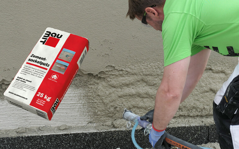 Der Sockel wird mit Zementsockelputz mit Hilfe einer Putzmaschine verputzt. Das Produktbild Zementsockelputz im roten Sack ist links aubgebildet.