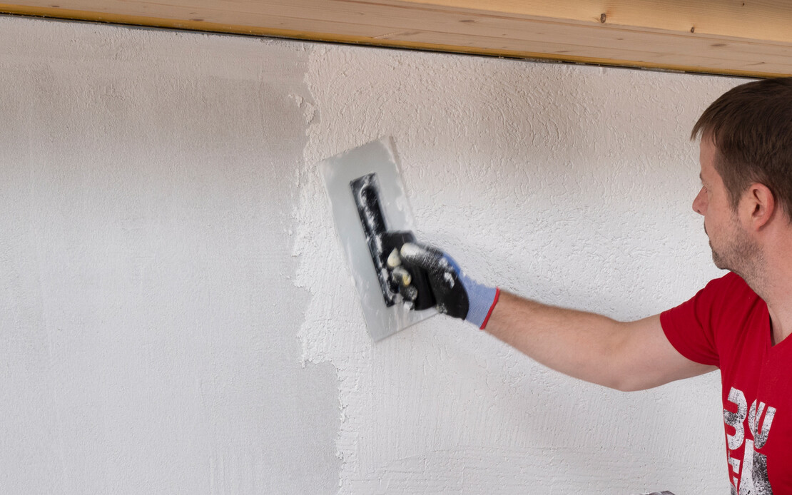 Mann verputzt eine Wand mit weißem Silikonharzputz.