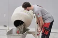Mann mischt Beton mit Betonmischer und füllt ihn in Schubkarre, Heimwerkerprojekt mit Baumit-Produkten.
