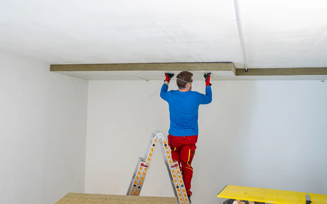 Heimwerker montiert Deckenverkleidung auf Leiter, Schritt-in-Schritt-Anleitung für DIY-Deckenrenovierung.