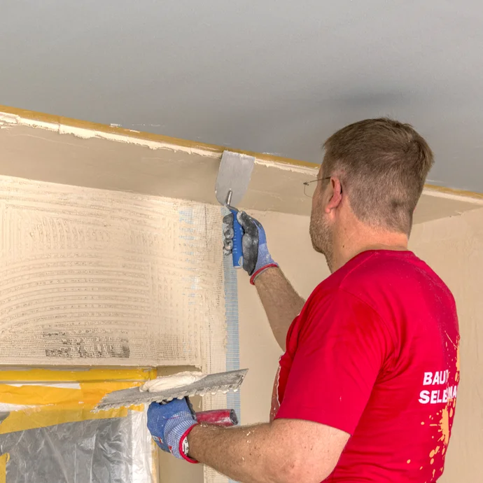Heimwerker glättet Putz an einer Wand mit einer Kelle. Anleitungen zur Wandrenovierung auf baumit-selbermachen.de.