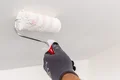 Maler grundiert eine Decke mit Farbrolle, Schritt für Schritt Anleitung für Heimwerker zur Deckenrenovierung.