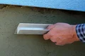 Hand glättet Putz an einer Wand mit einem Werkzeug für ebene Oberflächen, Heimwerkerprojekt für Außengestaltung.