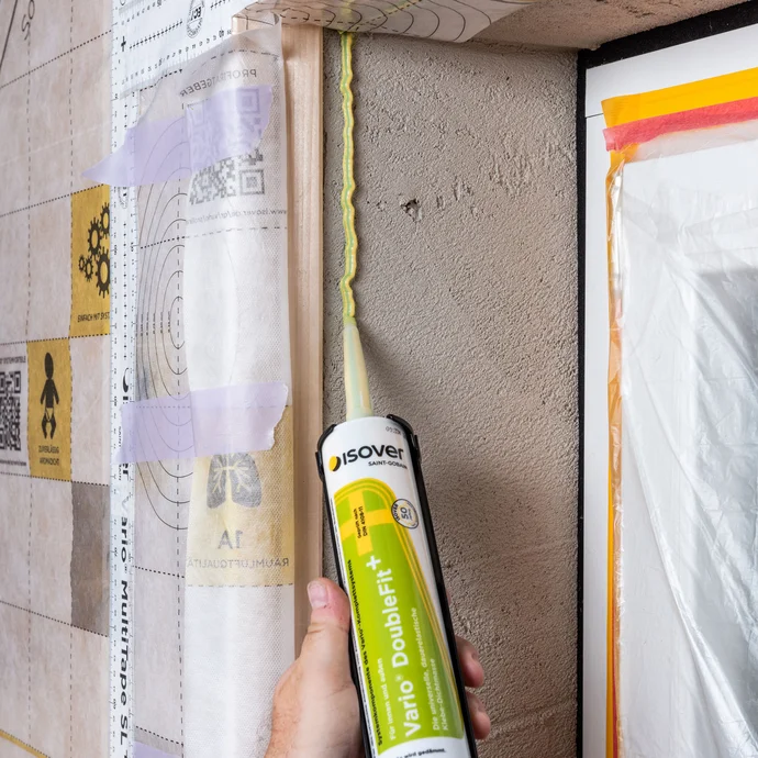 Die Vario DoubleFit+ Klebe-Dichtmasse von ISOVER wird auf der Laibung aufgetragen, um das Folienstück Dampfbremse anzukleben.
