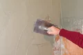 Heimwerker glättet Wand mit Kelle und Putz für gleichmäßige Oberfläche.