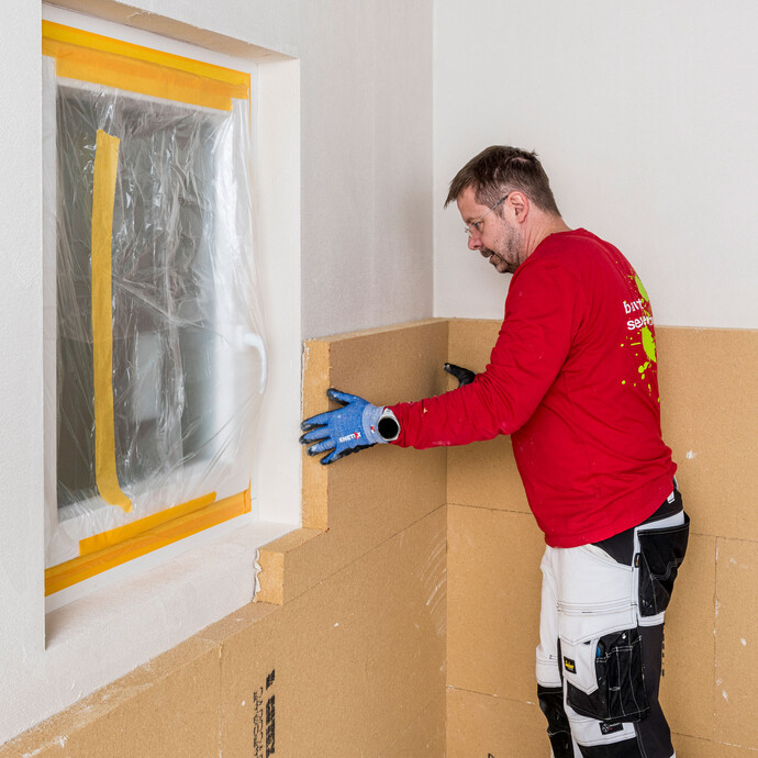 Die zugeschnittene Dämmplatte in L-Form für das Fenster wird mit Klebemörtel versehen und kräftig an die Wand geklebt. Baumit Selbermachen Anleitung Innenendämmung - geklebtes Mauerwerk.