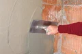 Auftragen von Putz an einer Ziegelwand mit einer Kelle, für ein glattes und gleichmäßiges Finish.