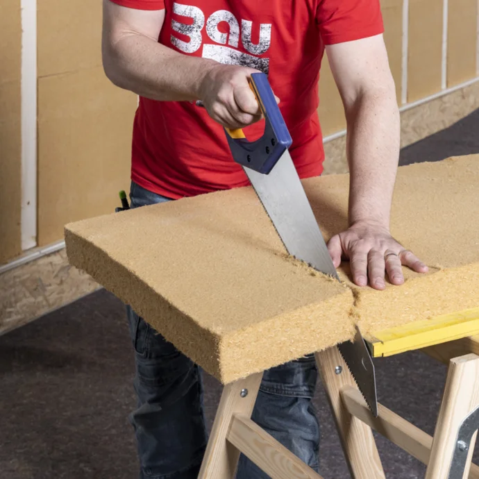 Mann schneidet Dämmplatte aus Steinwolle mit Säge, Vorbereitung zur Wärmedämmung, Heimwerkerprojekt, DIY-Anleitung für Baumit.