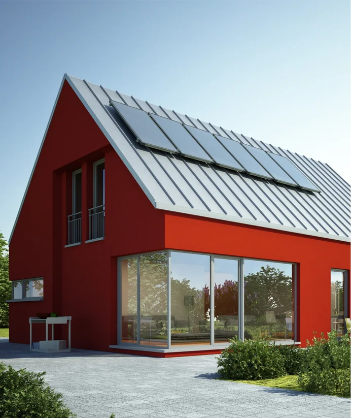 Modernes, rot gestrichenes Haus mit Solaranlage auf dem Dach, umgeben von üppigem Garten und klarem Himmel.