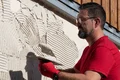 Heimwerker trägt Putz mit Kelle auf Fassade auf; Schritt-für-Schritt-Anleitung für Renovierung und Sanierung von Baumit.