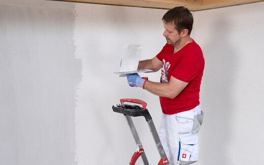 Person streift Reibebrett an Glättkelle ab, um überflüssiges Bindemittel zu entfernen.