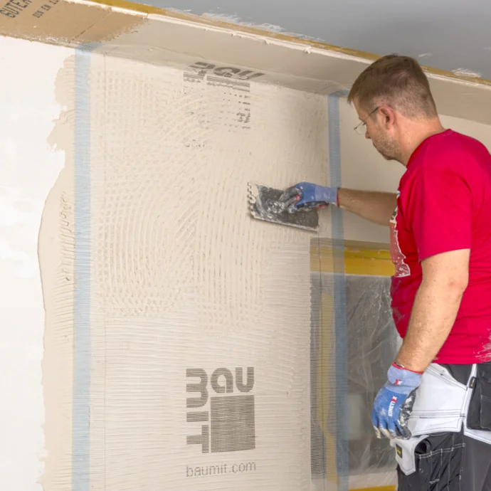 Heimwerker verspachtelt Wand mit Baumit-Putz in renoviertem Innenraum.