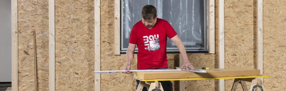Heimwerker misst D&auml;mmstoffplatte vor Holzrahmenbau ab.