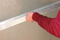 Hand zieht eine Abziehlatte über frisch aufgetragenen Putz an einer Wandoberfläche.